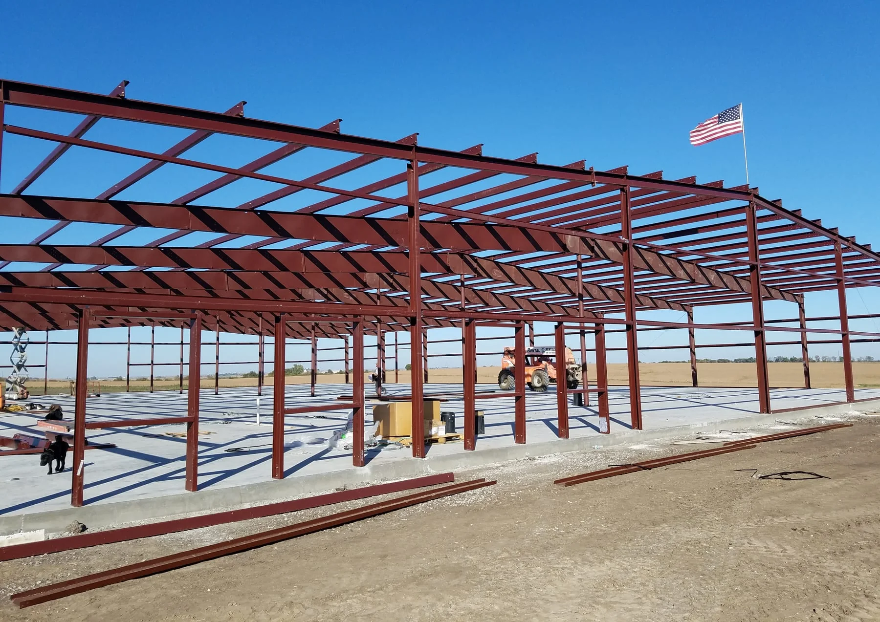 Representative archive field photo, not a matched project image: red steel framing under erection on a concrete slab with an american flag overhead